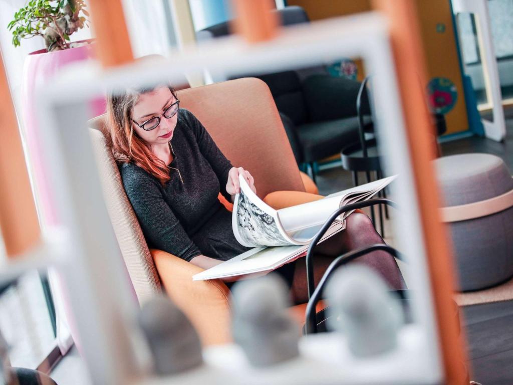 une femme assise sur une chaise en train de lire un journal dans l'établissement Novotel Suites Luxembourg, à Luxembourg