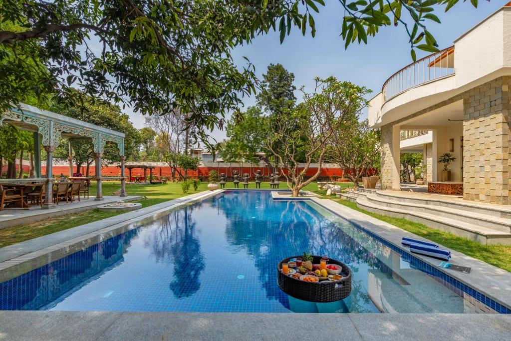 新德里的住宿－Elivaas Oasis Luxury 6BHK with Pvt Pool, Sainik Farm New Delhi，一座游泳池,旁边是一所房子,里面放着一碗水果