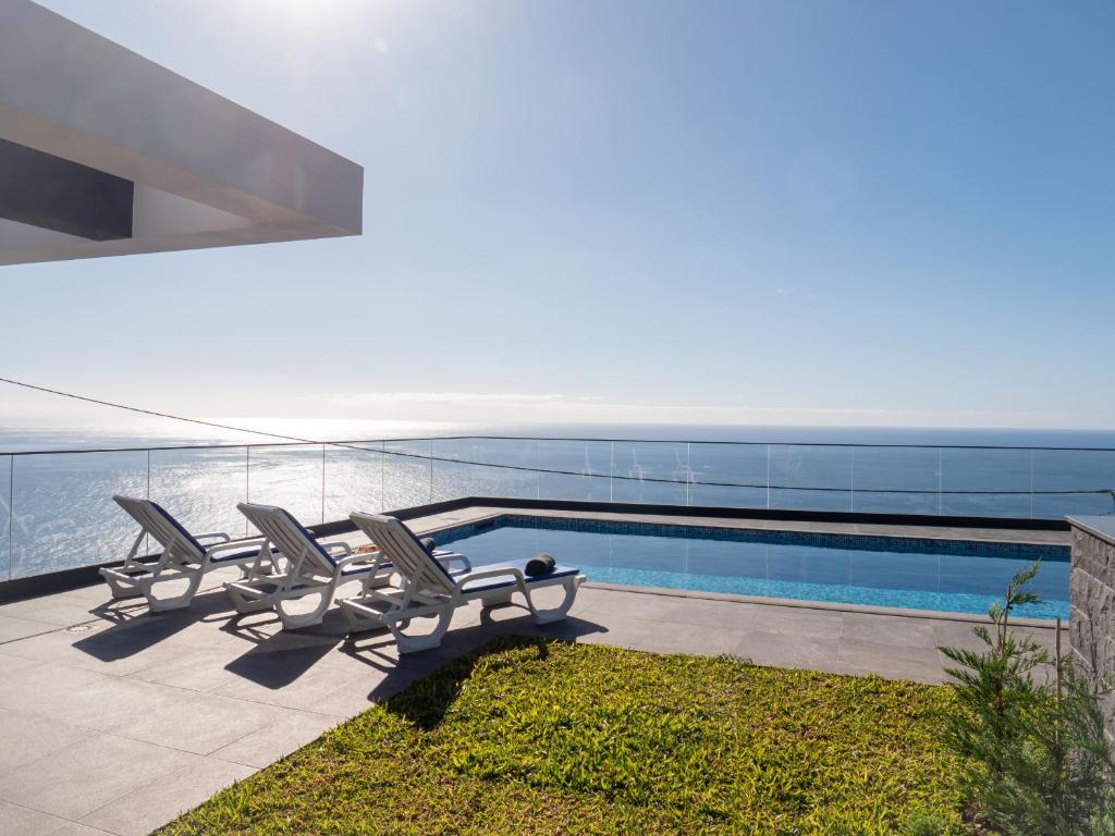 een zwembad met ligstoelen naast de oceaan bij Villa Luxe by Atlantic Holiday in Ribeira Brava