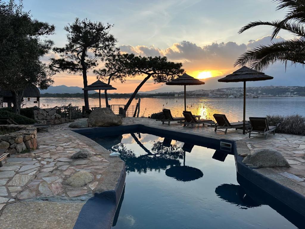 - une piscine avec des chaises et des parasols au coucher du soleil dans l'établissement Maranatha Résidence avec plage privée, piscine chauffée, à Porto-Vecchio