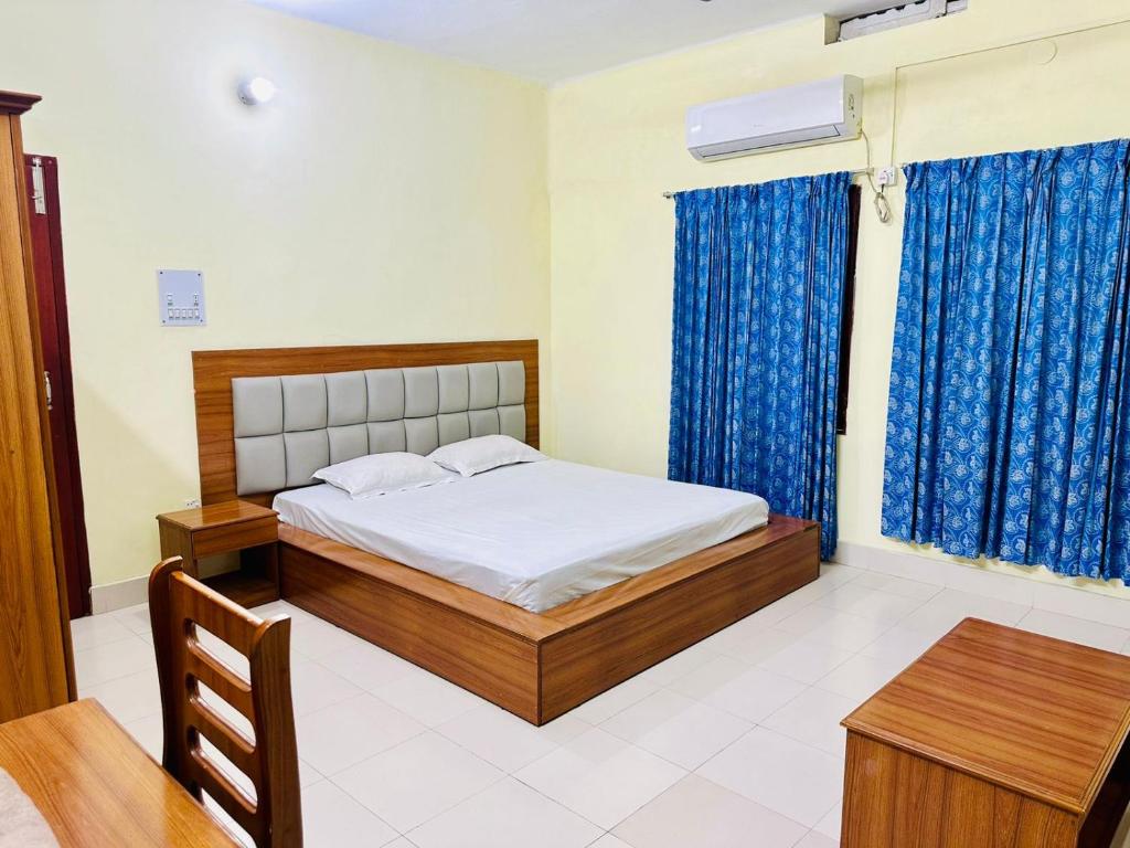 a bedroom with a bed with blue curtains and a table at Asroy Guest House in Dhopāgul