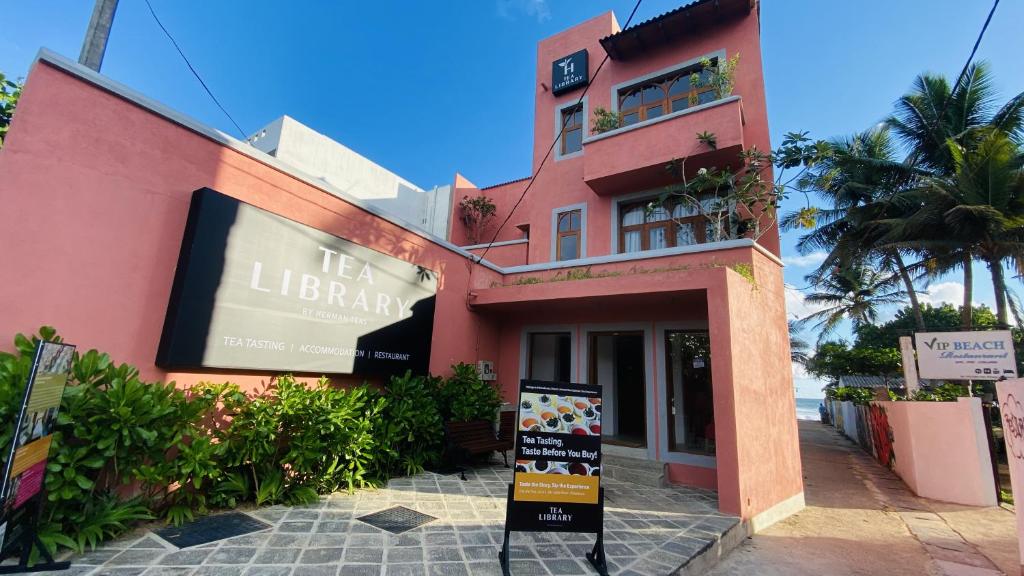 希克杜沃The Tea Library Hikkaduwa的粉红色的建筑,前面有标志