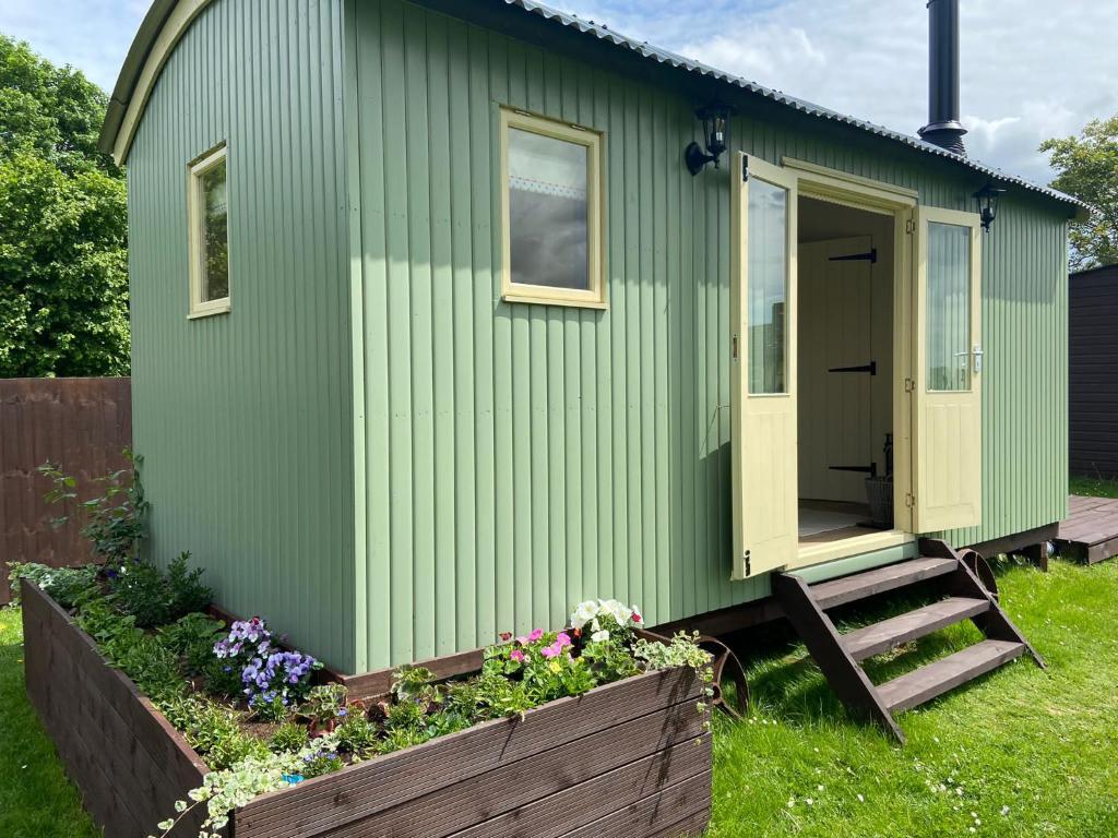 a green tiny house with a porch and flowers at Willow Shepherd Hut in West Row