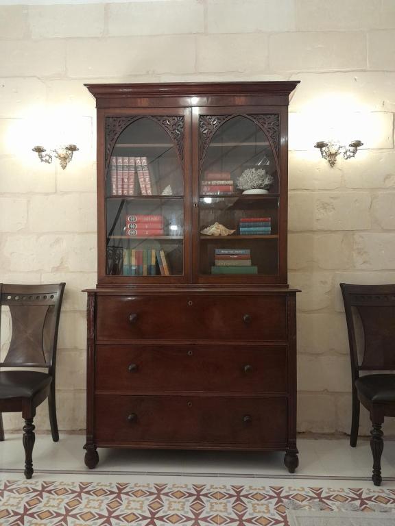 a wooden cabinet with books in it next to two chairs at Charming town house in Cospicua, Valperga Rooms in Cospicua