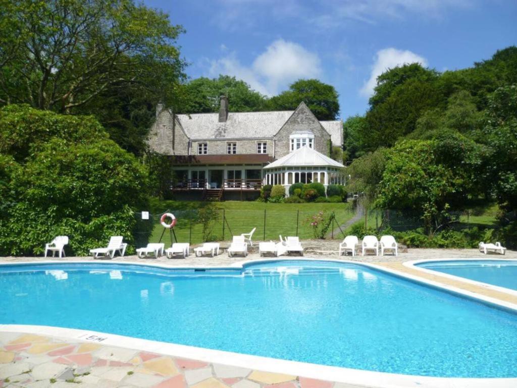 a swimming pool with chairs and a house in the background at 3 Bedroom Lodge Lanteglos 17 in Lanteglos