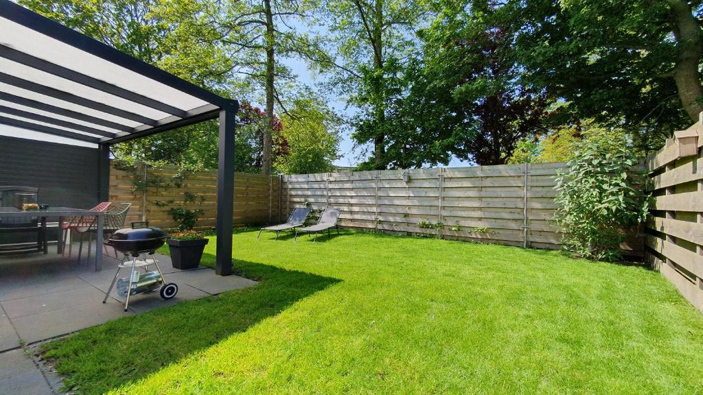 a backyard with a fence and a grill in the grass at Luxe vakantiebungalow Rust, Ruimte en Privacy in Dirkshorn