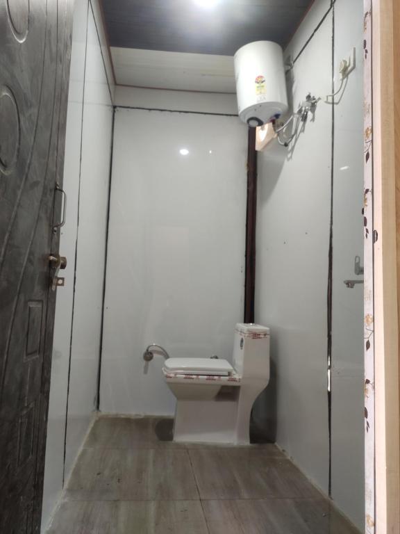 baño con aseo, luz y puerta en Hilans Hotel and Restaurant en Ukhimath