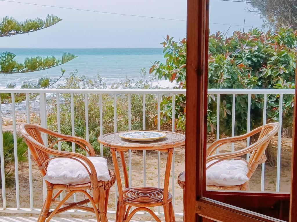 Una mesa y sillas en un balcón con la playa. en Casa Panarea - Villetta indipendente sul mare, en Marina di Modica