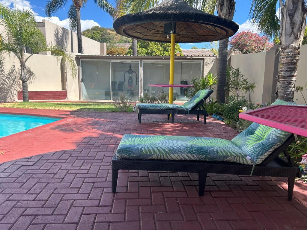zwei Stühle und ein Regenschirm neben einem Pool in der Unterkunft SiBella guest house in Bloemfontein