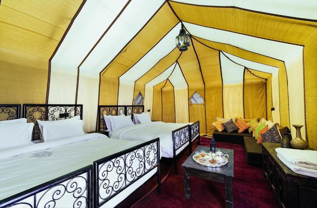 a room with two beds and a table in it at desert indigo luxury camp in Merzouga