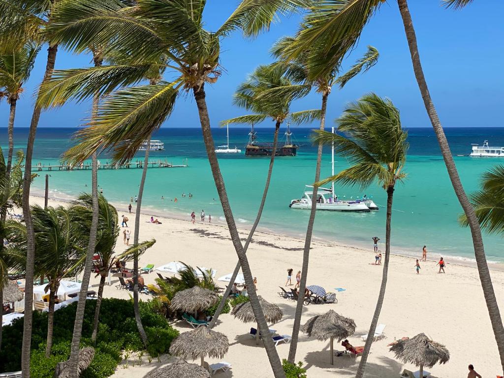 a beach with palm trees and people in the water at GRAND CARIBE BEACH CLUB and SPA - PLAYA LOS CORALES in Punta Cana