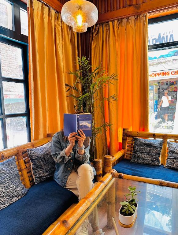 a person sitting on a couch reading a book at Drifters Inn - The Hidden Tribe in Manāli