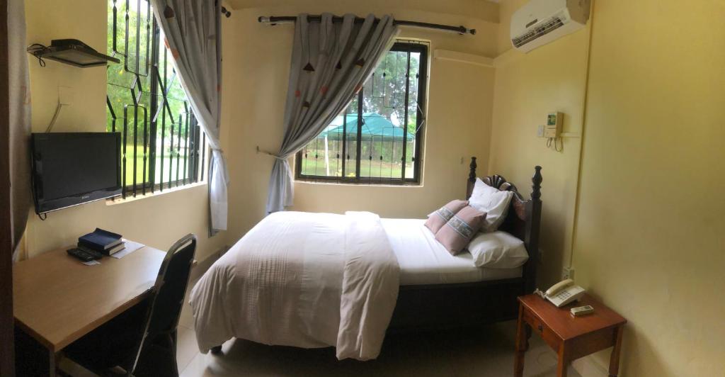a bedroom with a bed and a desk and two windows at CBA Hotel in Tanga