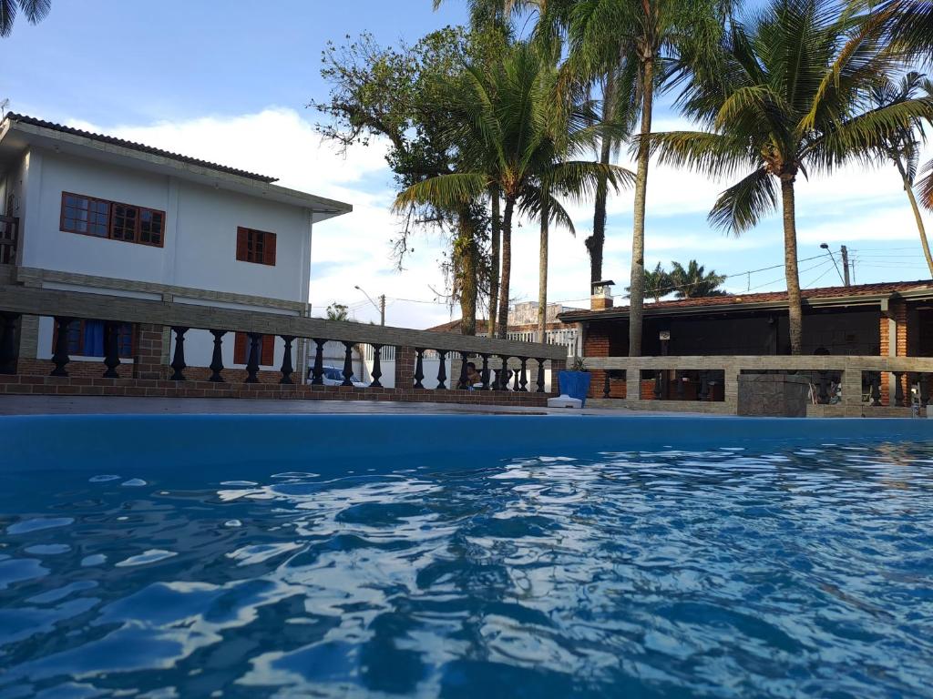 a swimming pool in front of a house with palm trees at Casarão Pertinho da Praia in Bertioga