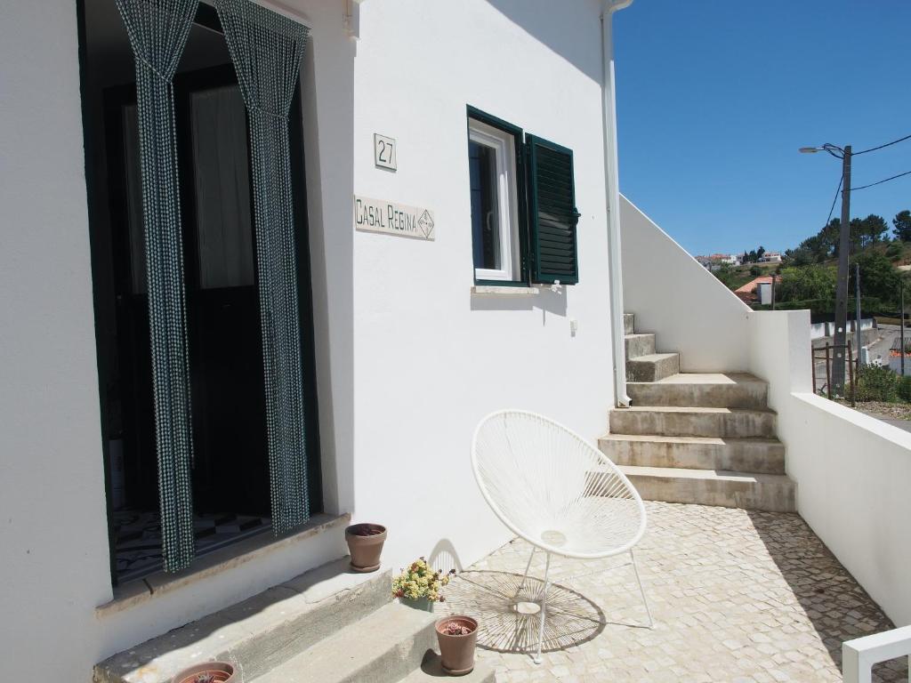 une maison blanche avec une chaise blanche sur une terrasse dans l'établissement Casal Regina, à Sesimbra
