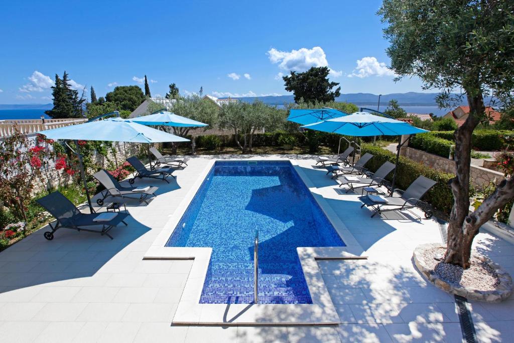 a swimming pool with chairs and umbrellas at Apartments Šemper - HEATED POOL in Bol