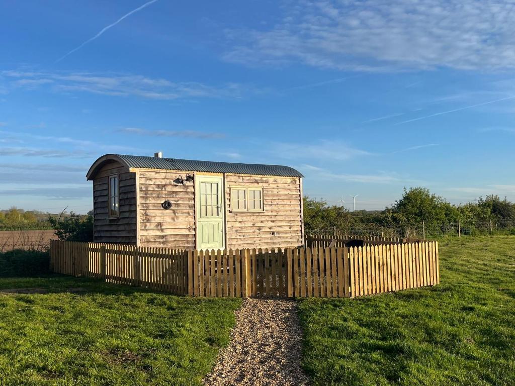 a small house behind a wooden fence in a field at Luxury Shepherd Hut in Kelham