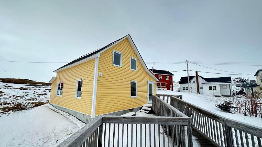 a yellow house with a fence in the snow at Victoria Cottage in Twillingate