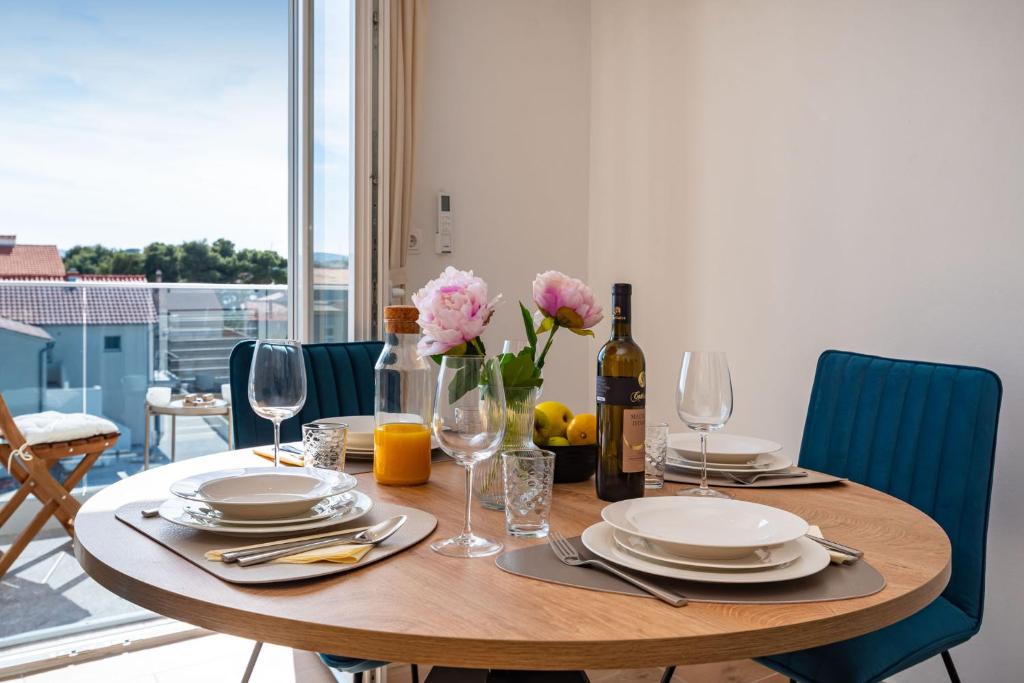 een houten tafel met borden en een fles wijn en bloemen bij Apartments Lucija Mari in Tribunj