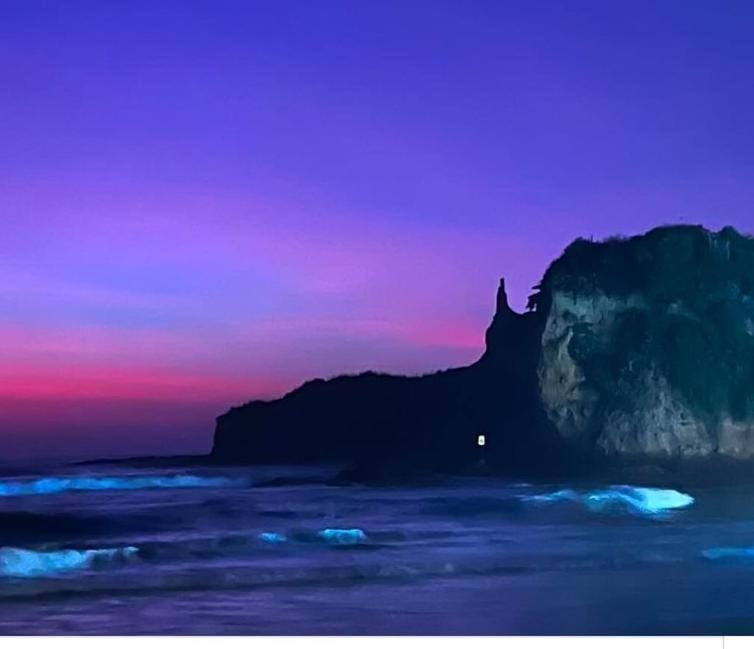een zonsondergang boven de oceaan met een rotsformatie bij Casa Bony in Montañita