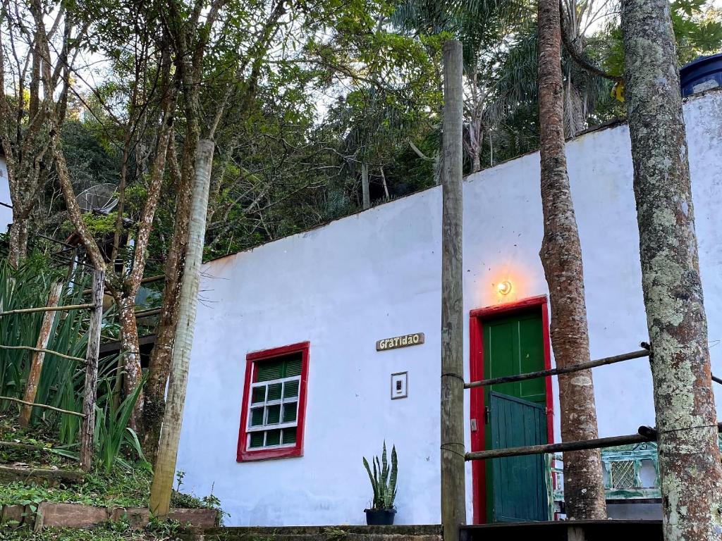 una casa bianca con una porta verde e alberi di Chalé na floresta com varanda a Ouro Preto