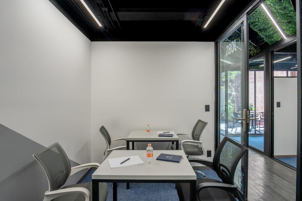 A small meeting room with two tables, office chairs, and glass doors opening toward a planted area.