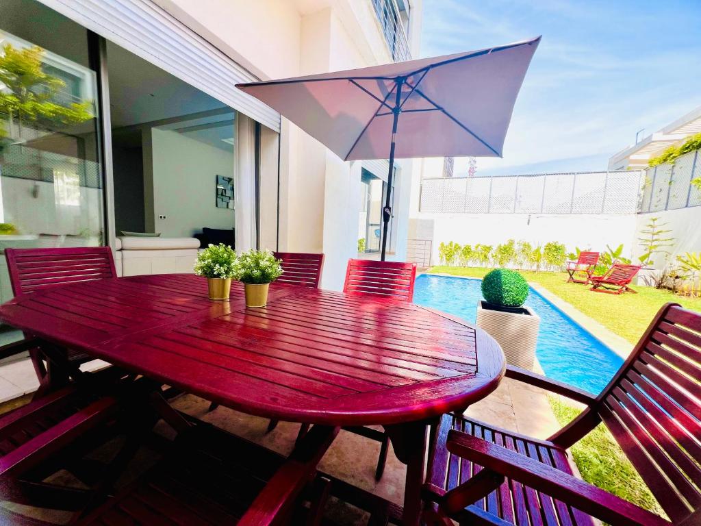 a red wooden table with chairs and an umbrella at luxury Villa with pool next mall in Dar Bouazza