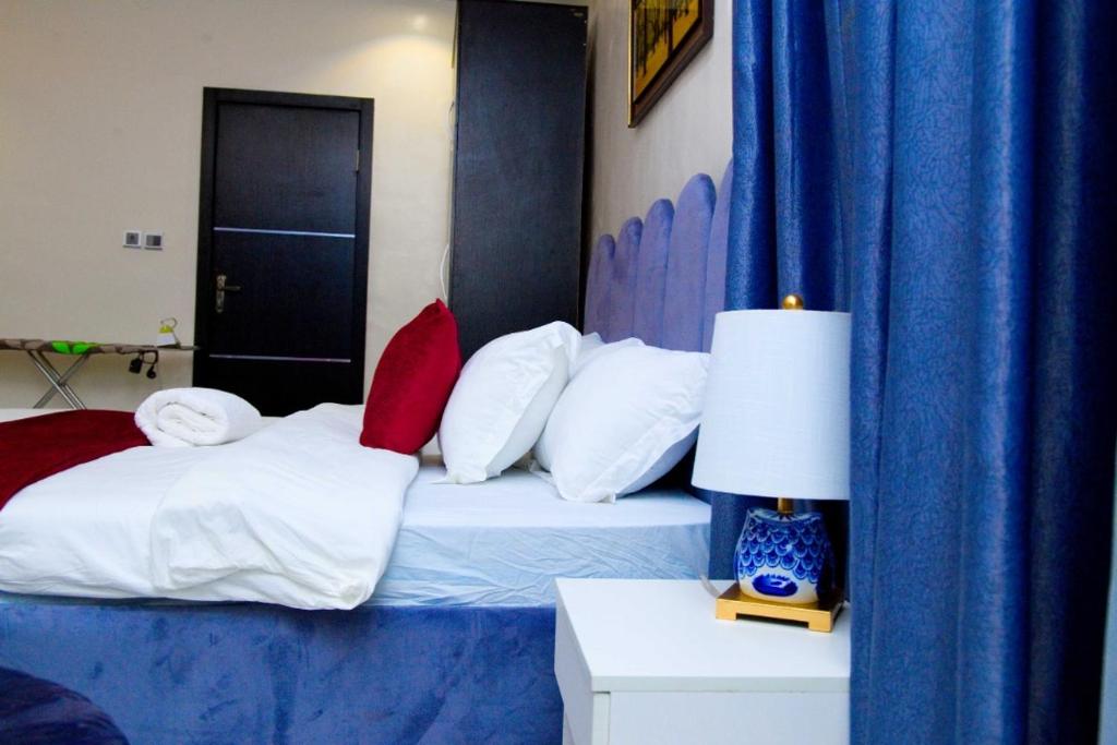 a bedroom with a bed with blue curtains and a lamp at D2 Studio Apartment in Lagos