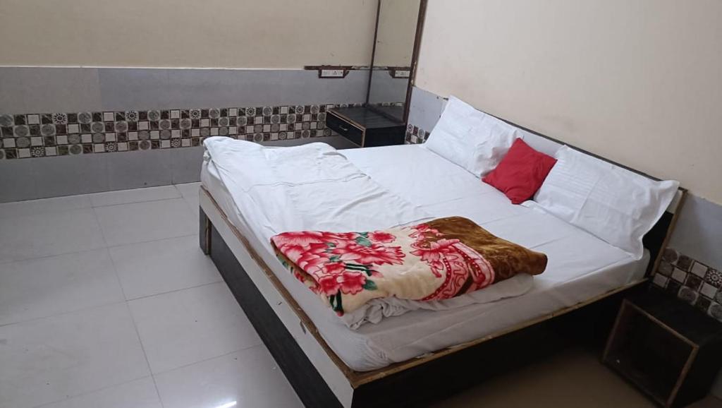 un letto con lenzuola bianche e un cuscino rosso di RESIDENCE TULSI a Vrindāvan