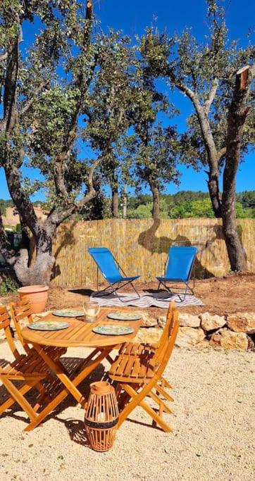 une table et des chaises en bois dans le sable près des arbres dans l'établissement Au p'tit soleil - Charmant T2 en Provence, à Barjols
