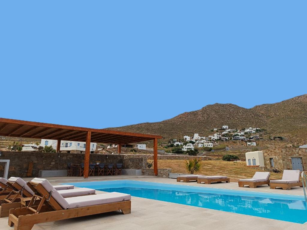 a swimming pool with lounge chairs and a mountain at Megusta Mykonos in Tourlos