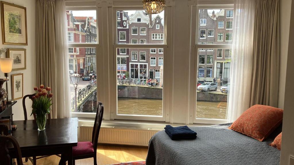 um quarto com uma cama, uma mesa e janelas em Canal View B&B Amsterdam em Amsterdã