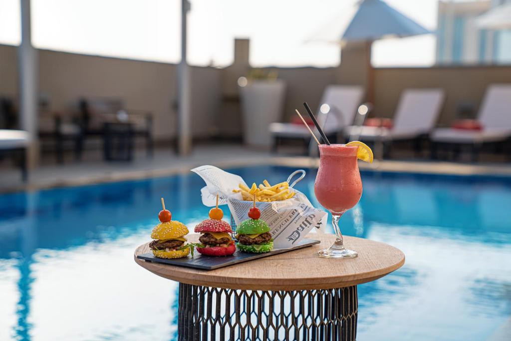 a tray of food and a drink next to a pool at Centro Al Manhal by Rotana in Abu Dhabi