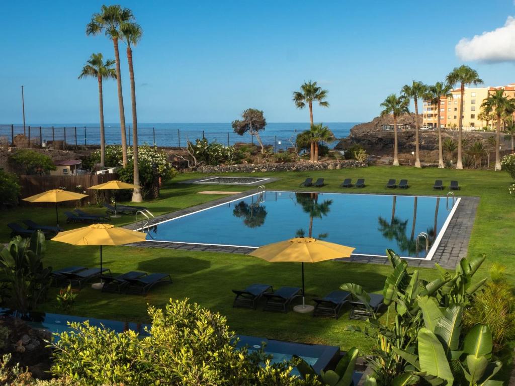 Blick auf einen Pool mit Sonnenschirmen und das Meer in der Unterkunft 11 Holiday Homes in San Miguel de Abona