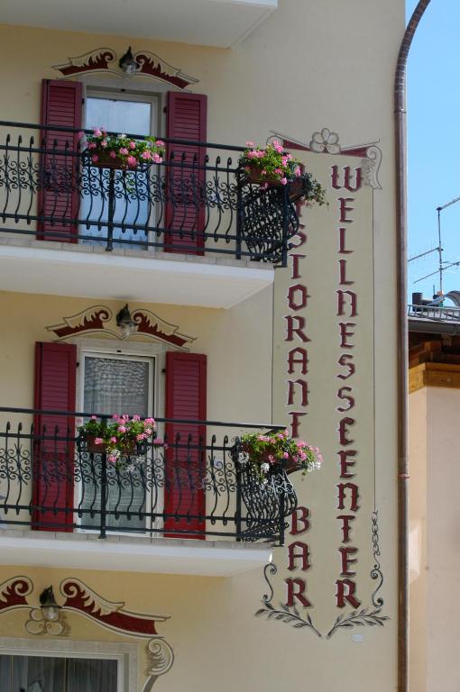a building with red doors and balconies with flowers at Hotel Paganella, Tradition In Hospitality in Fai della Paganella