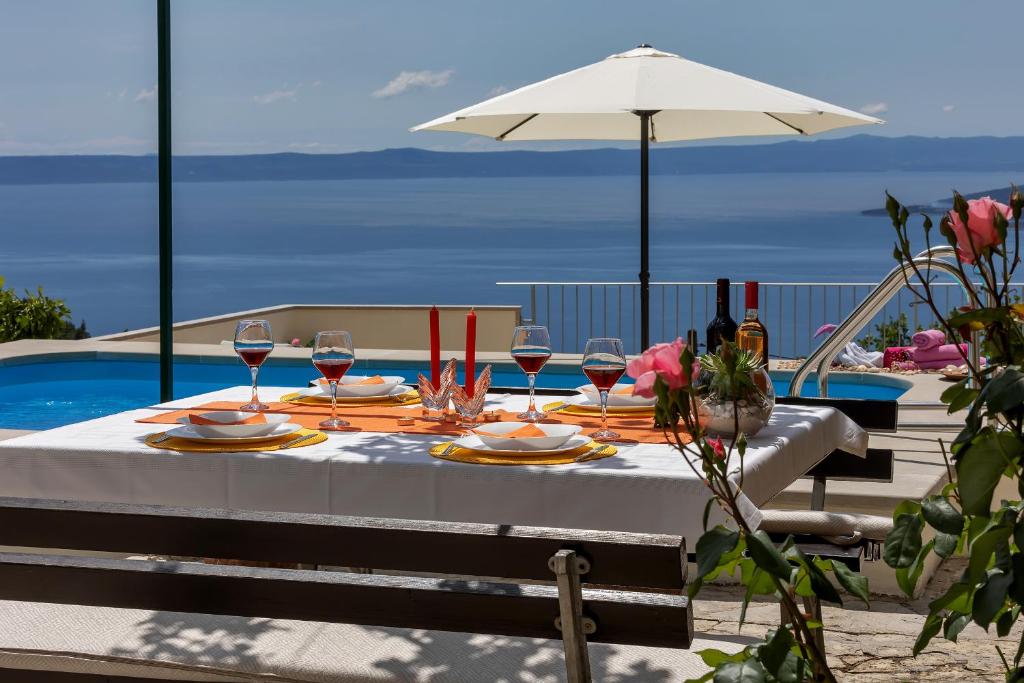 a table with wine glasses and an umbrella next to a pool at Holiday home Marta with heated pool,grill,sea view in Bast