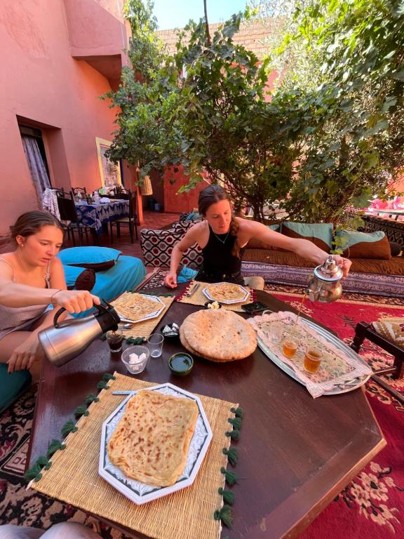 zwei Frauen sitzen um einen Holztisch mit Essen drauf in der Unterkunft Dar Toda - Zagora guest house in Zagora