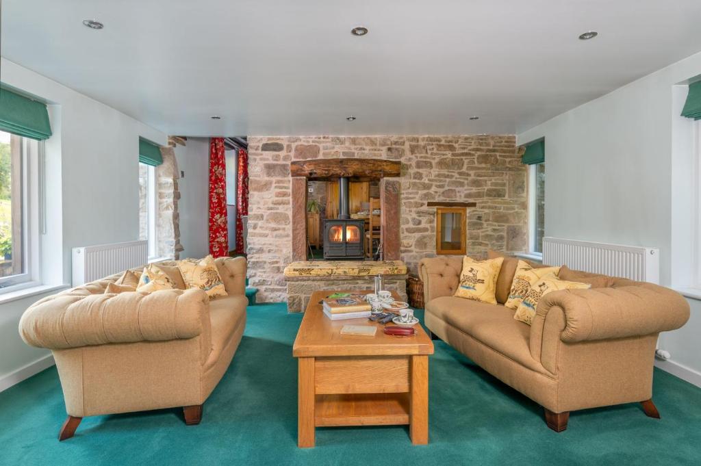 a living room with two couches and a stone fireplace at The Gardeners Cottage, Hutton John is a luxurious cottage with hot tub 10 minutes from Lake Ullswater in Penruddock