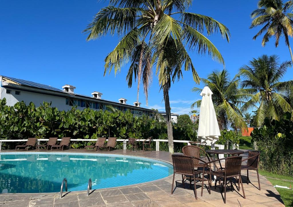 a pool with chairs and a umbrella and palm trees at Apto/Hotel Praia Taperapuã - Beira Mar in Porto Seguro