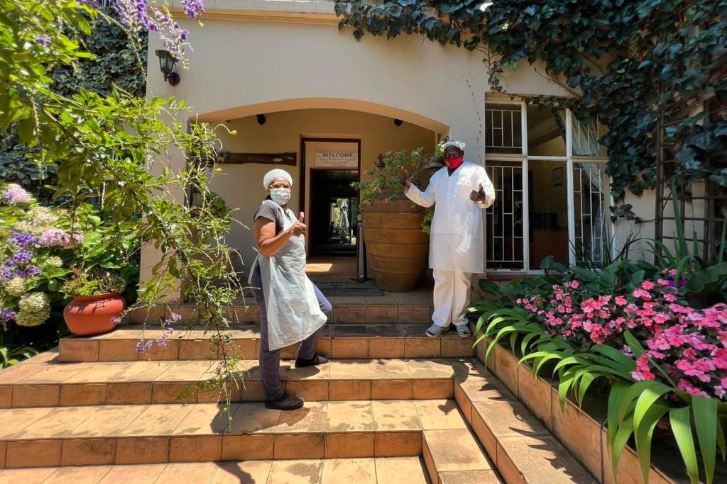 zwei Personen stehen vor einem Haus mit Blumen in der Unterkunft Ipe Tombe Guest Lodge - Midrand in Midrand