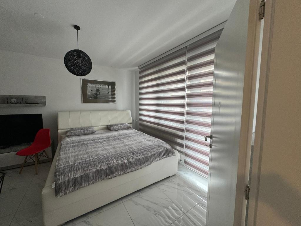 a white bedroom with a bed and a red chair at Apartman City Center 2 in Prijedor