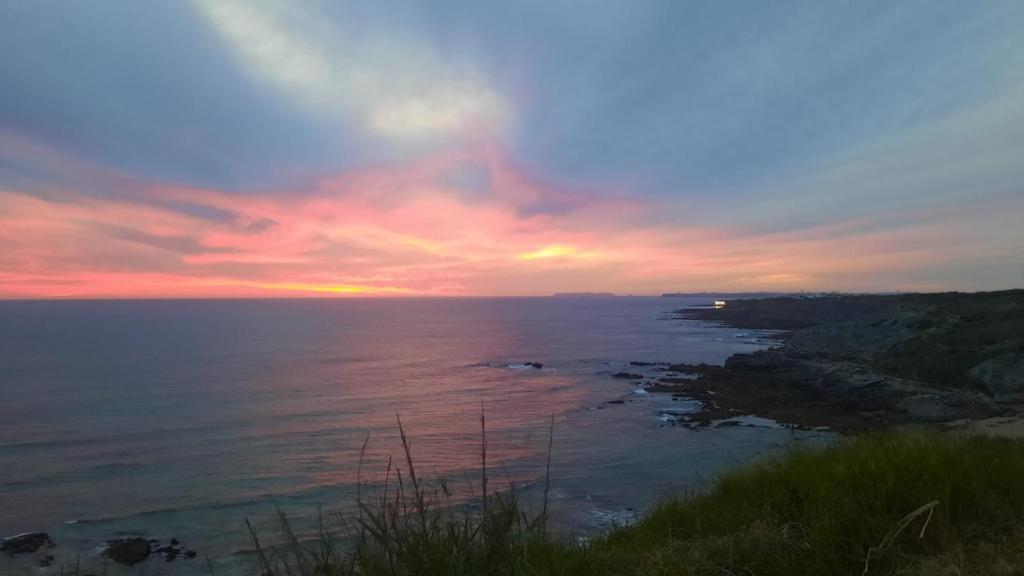 um pôr-do-sol sobre um corpo de água com o oceano em The Whale Beach House em Atouguia da Baleia