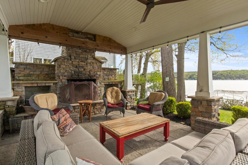 a porch with a stone fireplace and chairs and a table at Luxury Conesus Lakeside Dock Modern Amenities in Livonia