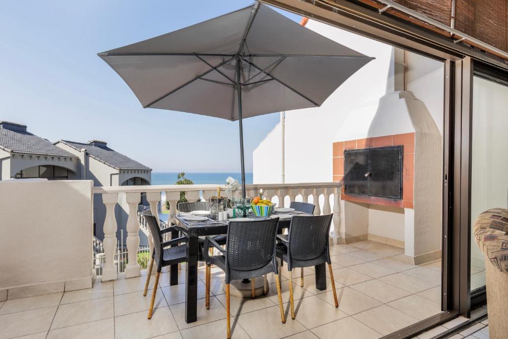 una mesa y sillas con una sombrilla en el balcón en Uvongo Cabanas 15B, en Margate