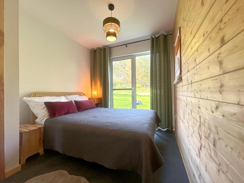 a bedroom with a bed and a large window at Żywiołowo - domki w stylu stodoły z placem zabaw i stawem - ZIEMIA in Parchowo