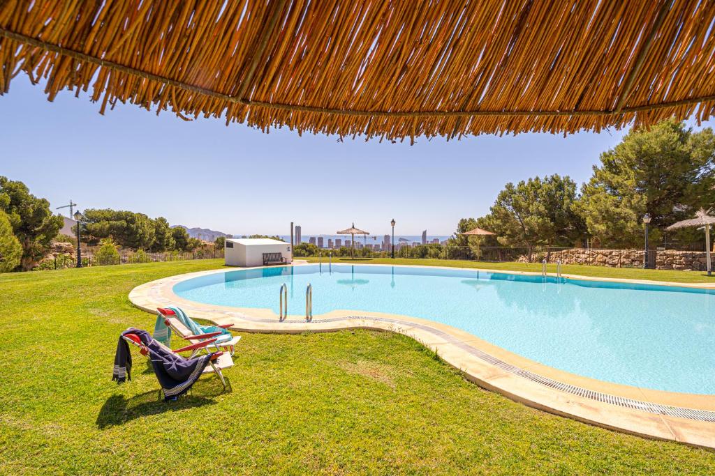 a swimming pool with two lawn chairs and a straw umbrella at Bahia Vista - Chalet adosado con vista al mar in Finestrat