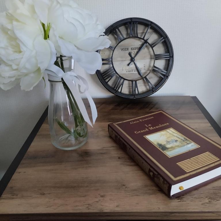 une table avec un livre et une horloge et un vase avec des fleurs dans l'établissement Maison de village en Périgord, à Singleyrac