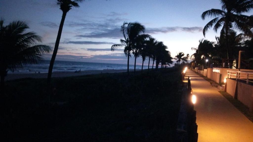 a street with palm trees and the beach at night at Casa do Sossego Guarajuba Barra do Jacuípe in Camaçari