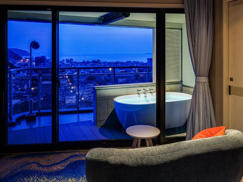 a bathroom with a tub and a view of the city at Ito Hotel Juraku in Ito