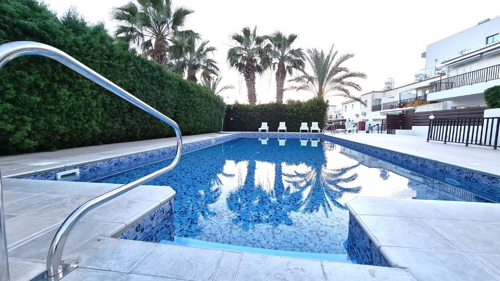 a swimming pool with chairs and palm trees at Kings Bungalow in Paphos